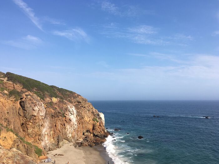 Cliffside view of the ocean with rocky shoreline and clear blue skies, showcasing amazing views from coastal states.