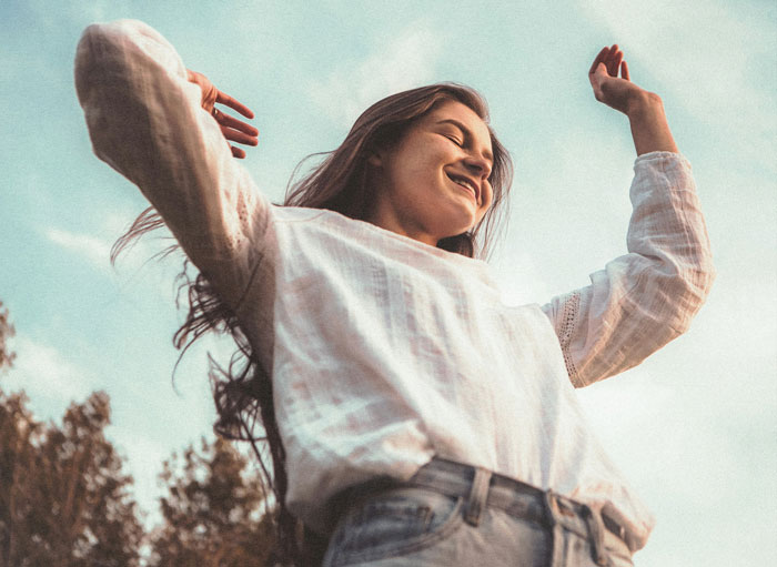 Woman celebrating sobriety milestone outdoors, looking joyful with arms raised against a blue sky. Woman celebrating sobriety milestone outdoors, looking joyful with arms raised against a blue sky.