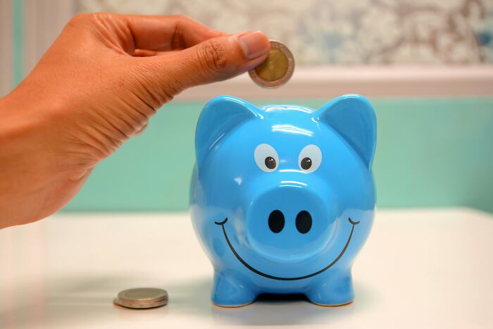 Hand placing coin into a blue piggy bank, symbolizing outdated financial stereotypes.