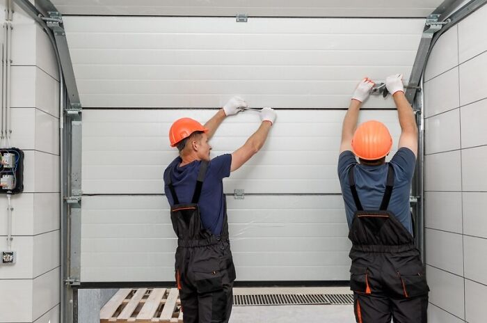 Workers in hard hats and overalls installing a garage door, illustrating that everyday things might seem harmless but could be dangerous.
