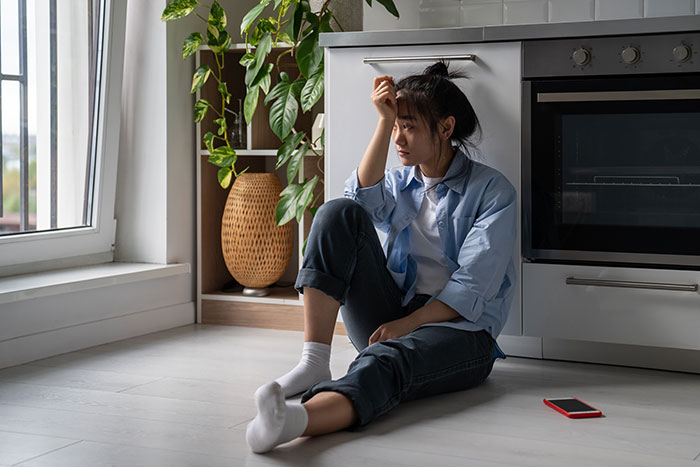Woman looking shocked, sitting on kitchen floor beside a plant, reflecting on boyfriend's fictitious friend group. Woman looking shocked, sitting on kitchen floor beside a plant, reflecting on boyfriend's fictitious friend group.