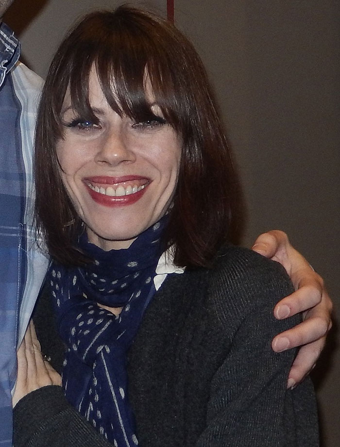 Individual smiling in a dark sweater and blue scarf, representing a celebrity who lost fame.