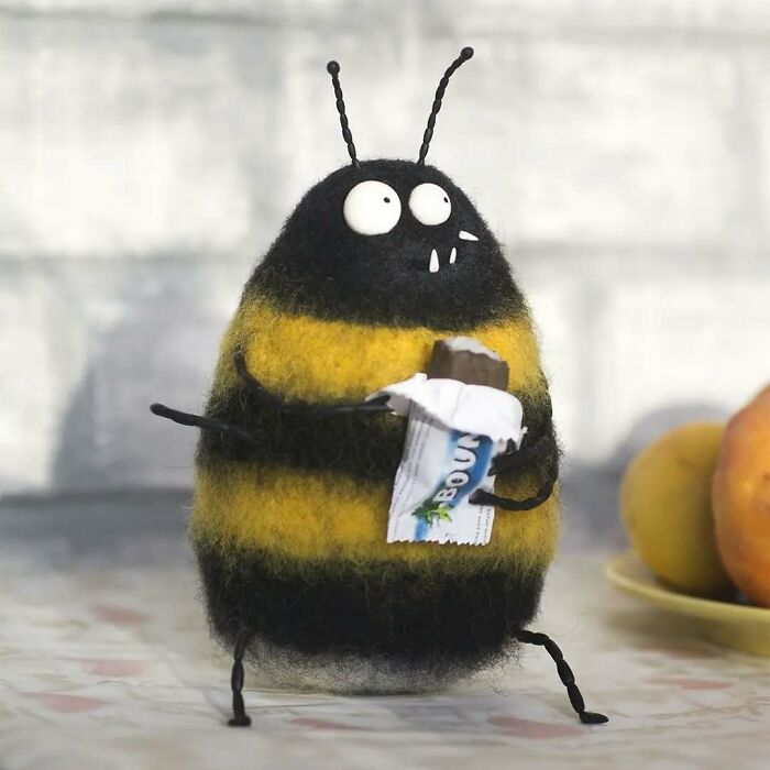 Strange art doll of a bee with a quirky expression holding a candy bar.