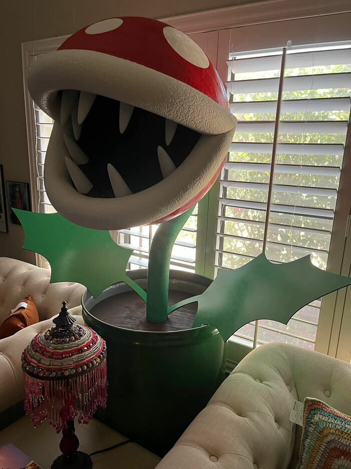 Giant plant sculpture with sharp teeth in a cozy room, a secondhand find, near a vibrant vintage lamp.