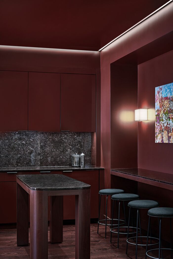 Award-winning interior design featuring deep red tones, a sleek bar counter, dark stools, and modern art on the wall.