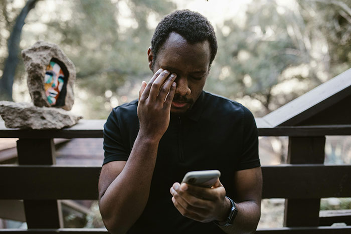 Man looking stressed while reading something on his phone, outdoors.