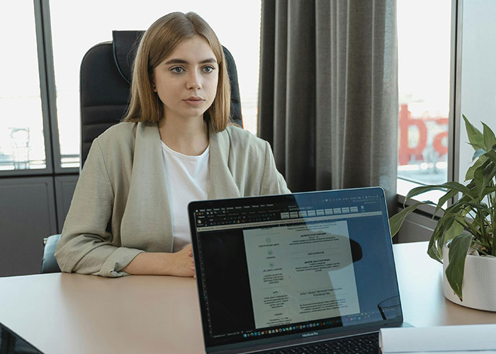 Young woman at a desk, nervously awaiting an awkward job interview, with a laptop showing her resume.