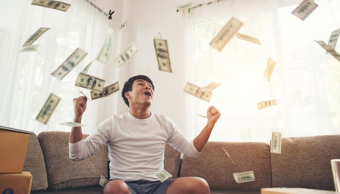 Person on a couch surrounded by falling money, illustrating outdated financial stereotypes.