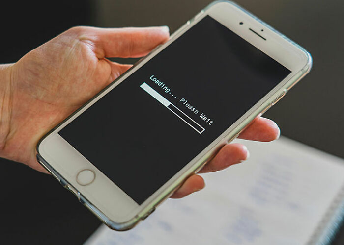 Hand holding a smartphone displaying a loading screen with a progress bar and message "Loading... Please Wait."
