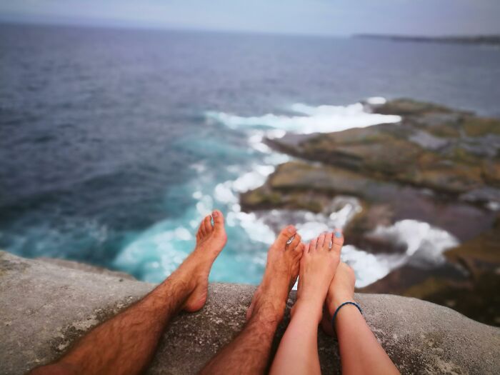 Feet dangling over a cliff edge above the ocean, illustrating a potentially dangerous everyday activity.