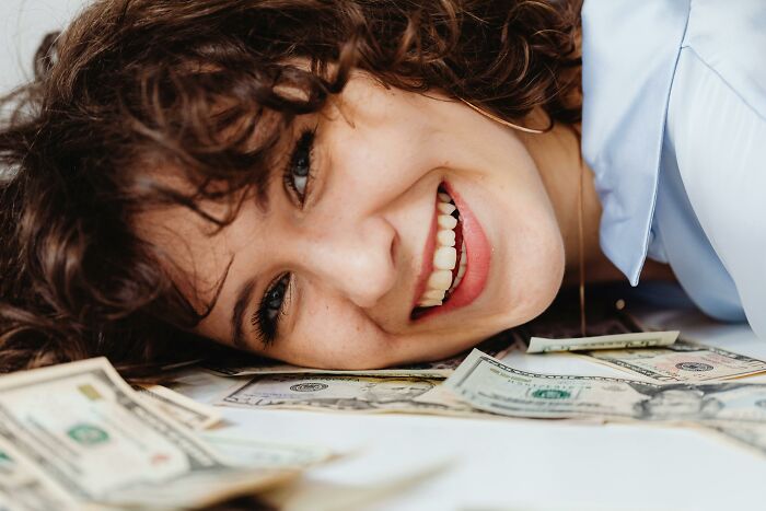 Smiling woman lying on dollar bills, symbolizing adult realizations about money and life.
