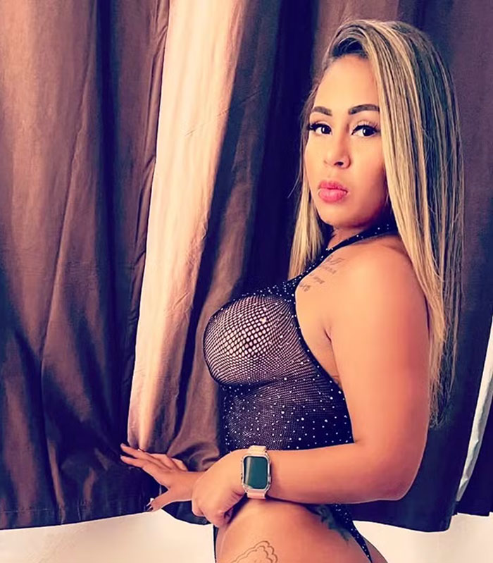 Adult star posing in a revealing outfit near curtains.