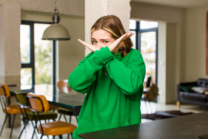 Young woman in green sweater showing refusal gesture indoors, illustrating facts you weren’t taught in school about the past.