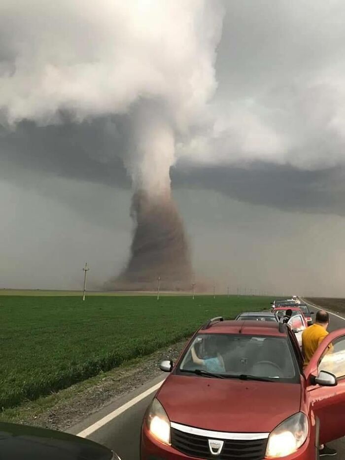 Cars on a roadside stopped to observe a massive tornado, highlighting nature disaster resilience.