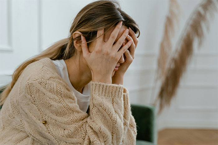 Woman looking distressed in her home, covering her face with her hands, with a focus on stains allusion.