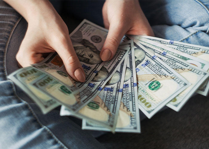 Person holding several hundred-dollar bills, illustrating finance and income combining for married couples.
