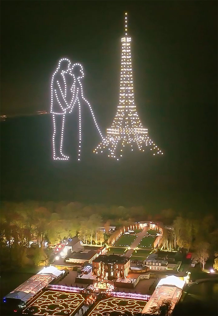 Drone light show above lavish wedding venue at night, highlighting a bride and Eiffel Tower.