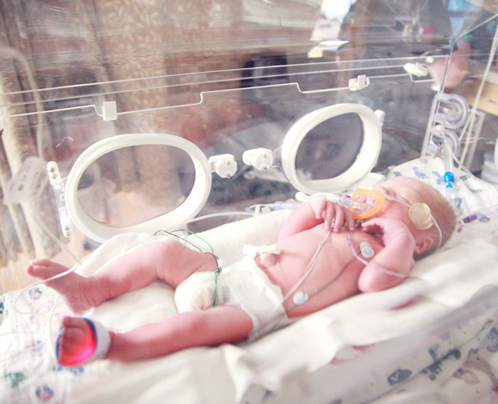 Newborn baby in an incubator, representing sacrifice and survival stories.
