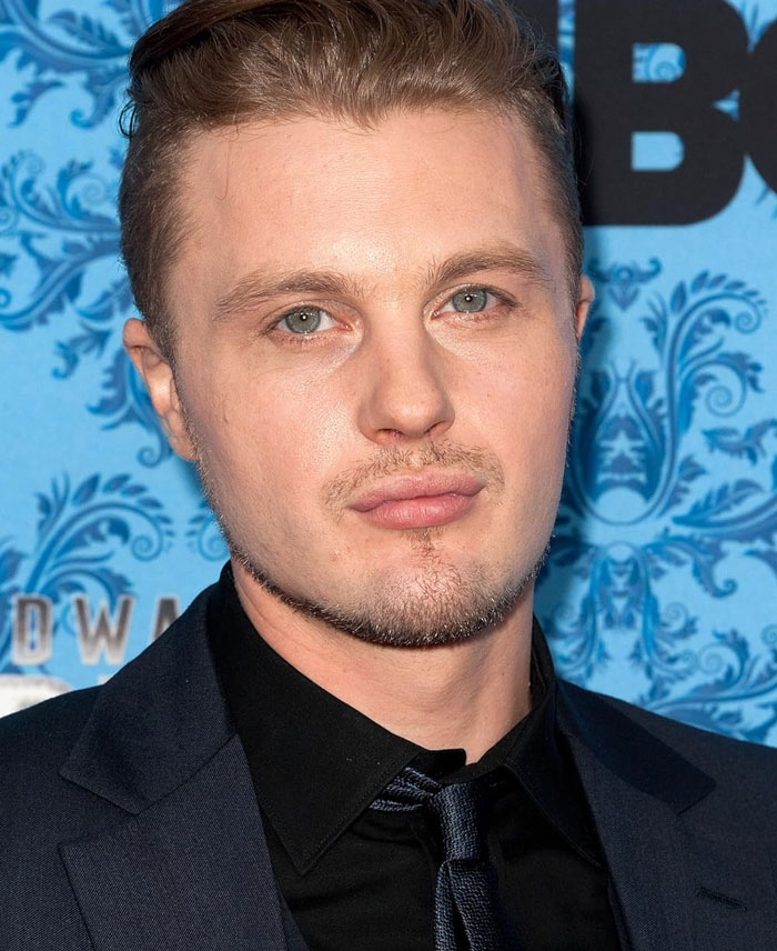 A celebrity, once famous, wearing a suit at a public event with a patterned blue background.