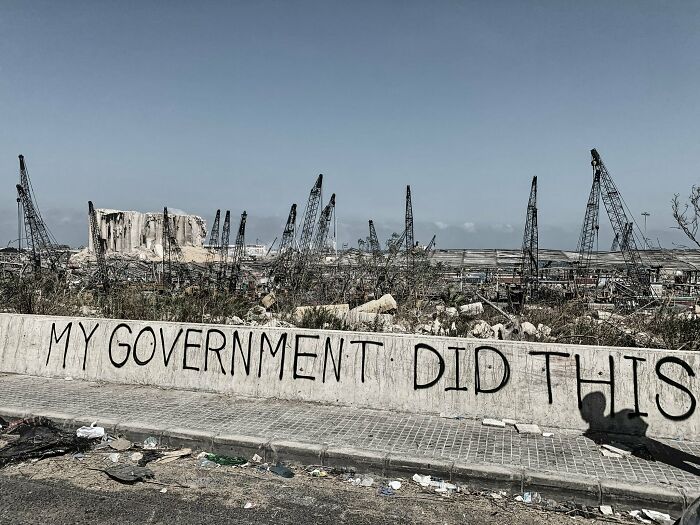 Urban hell scene with graffiti saying "My government did this," showing desolate industrial ruins and cranes.
