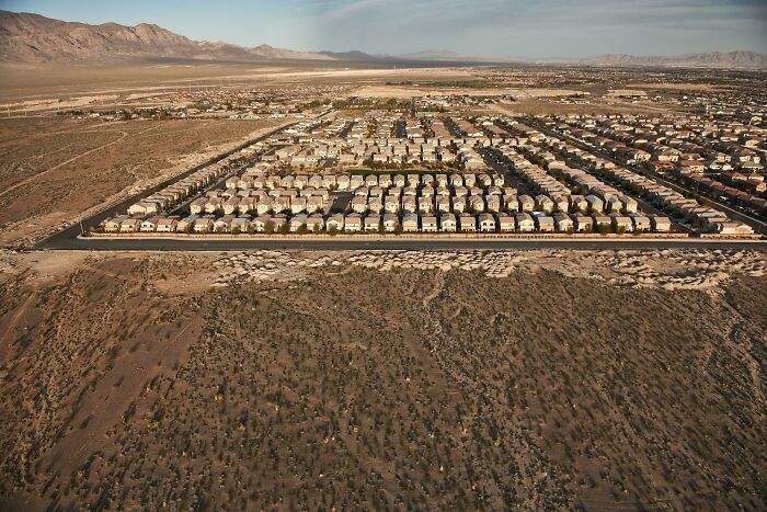 Aerial view of urban sprawl showcasing rows of identical houses in a dry landscape, illustrating urban hell concept.