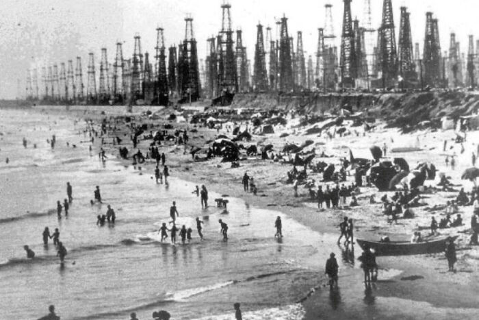 Crowded beach with numerous oil rigs in the background, depicting urban hell.