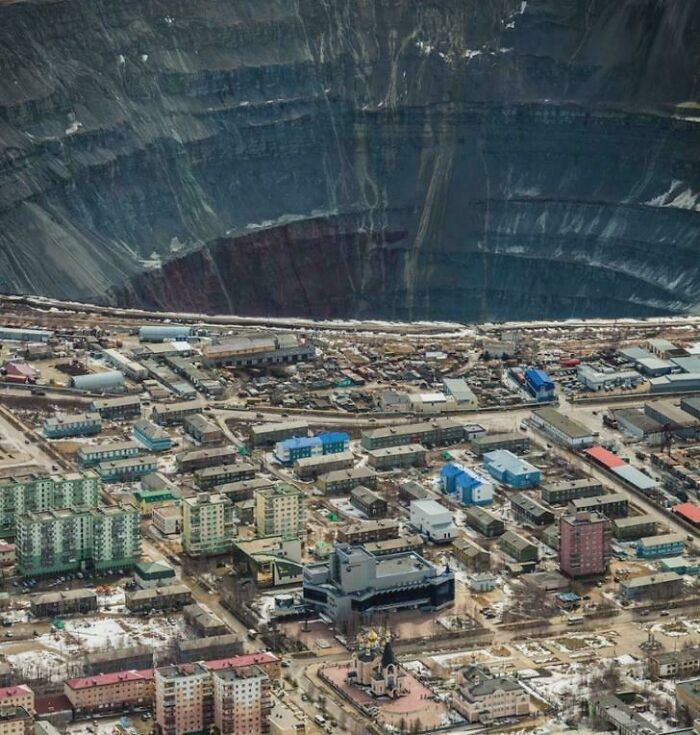 Bird's eye view of an urban area with a massive open pit mine nearby, illustrating urban hell.