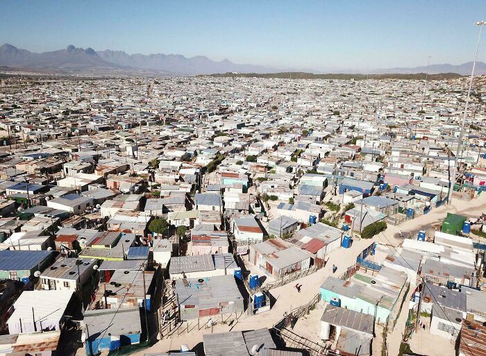 Aerial view of a vast urban landscape filled with densely packed, makeshift homes under a clear sky.