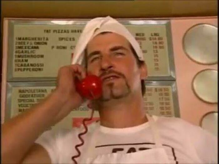 Man in chef hat on red phone, menu board background; funny moment from 'Nope' community in Australia.