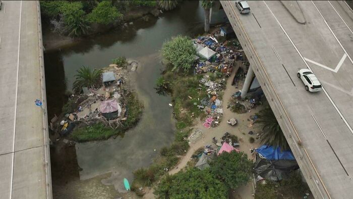 Aerial view of urban hell with tents and debris under a highway overpass, illustrating harsh city living conditions.