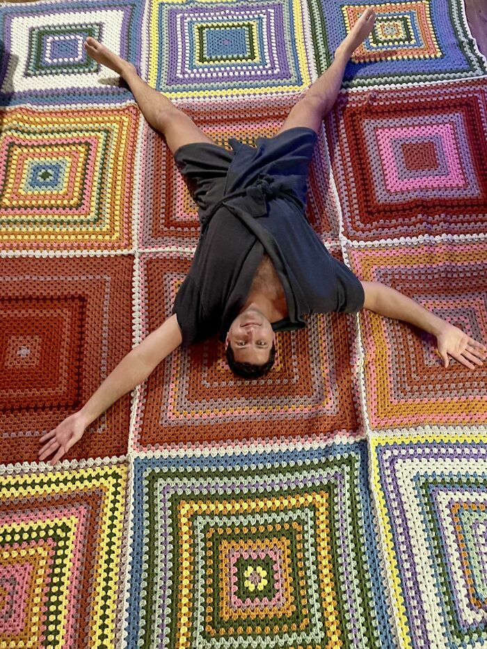 Man lying on colorful crocheted blanket made of large granny squares, showing proud crochet enthusiasts project.