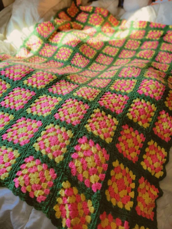 Colorful crochet blanket with pink and yellow squares bordered in green, showcasing a proud crochet enthusiast’s handmade project.