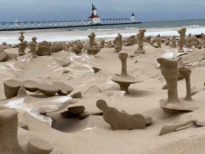 Unique sand formations on a beach with a lighthouse in the background, showcasing fascinating natural phenomena.