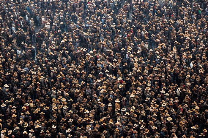 A vast crowd of people wearing similar hats, depicting the symphonic chaos of modernity.