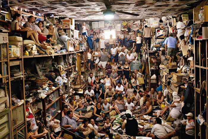 A crowded room filled with people, surrounded by clutter, illustrating the symphonic chaos of modernity.
