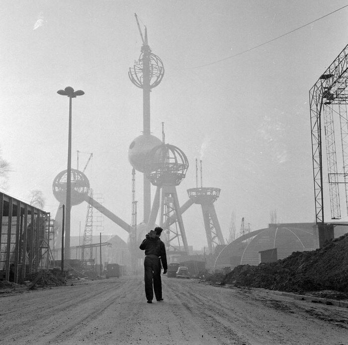 Worker walking towards under-construction Atomium, a fascinating historical landmark, with cranes in the background.