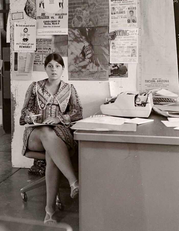 Woman in a retro office setting with a typewriter and boxing posters, highlighting fascinating historical pics.