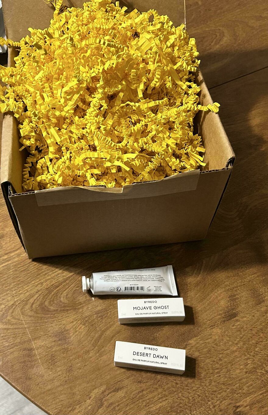 Box with excessive yellow crinkle paper and small perfume samples, highlighting wasteful unnecessary packaging.