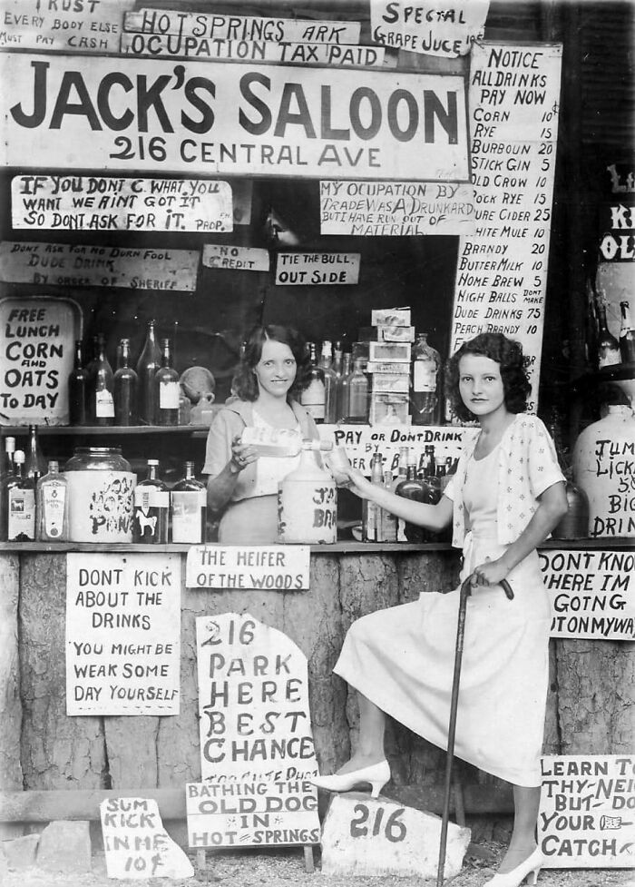 Two women stand at Jack's Saloon booth with humorous signs, showcasing fascinating historical pics.
