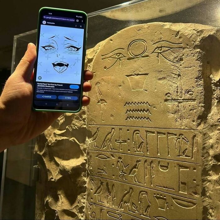 Hand holding a smartphone with an anime face overlaid on ancient hieroglyphs, highlighting weirdness.