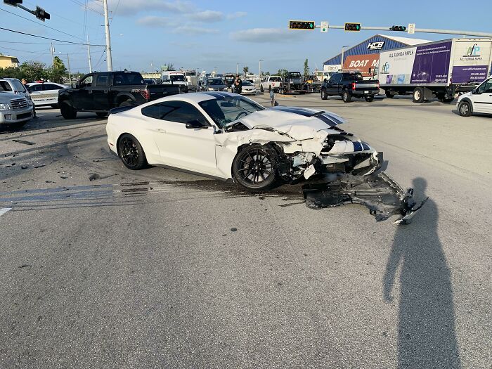 Damaged white car in a traffic accident scene, highlighting dangerous driving behavior on a busy road.