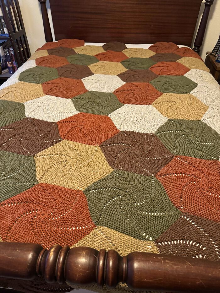 Crochet enthusiasts’ colorful hexagon blanket displayed neatly on a wooden bed frame in a cozy bedroom.