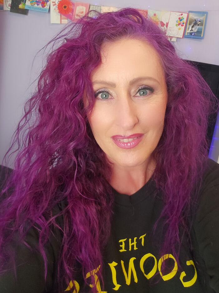 Woman with vibrant purple hair smiles, showcasing changing hair color styling.