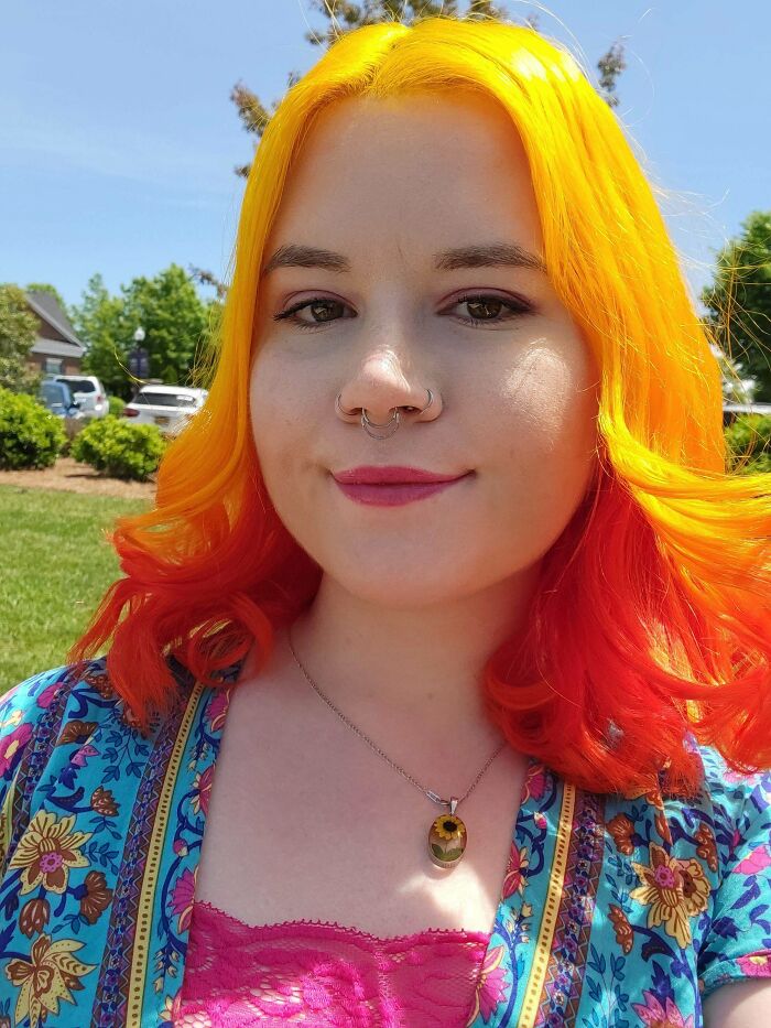 Person with vibrant changing-hair-color, wearing a colorful outfit and standing outdoors.