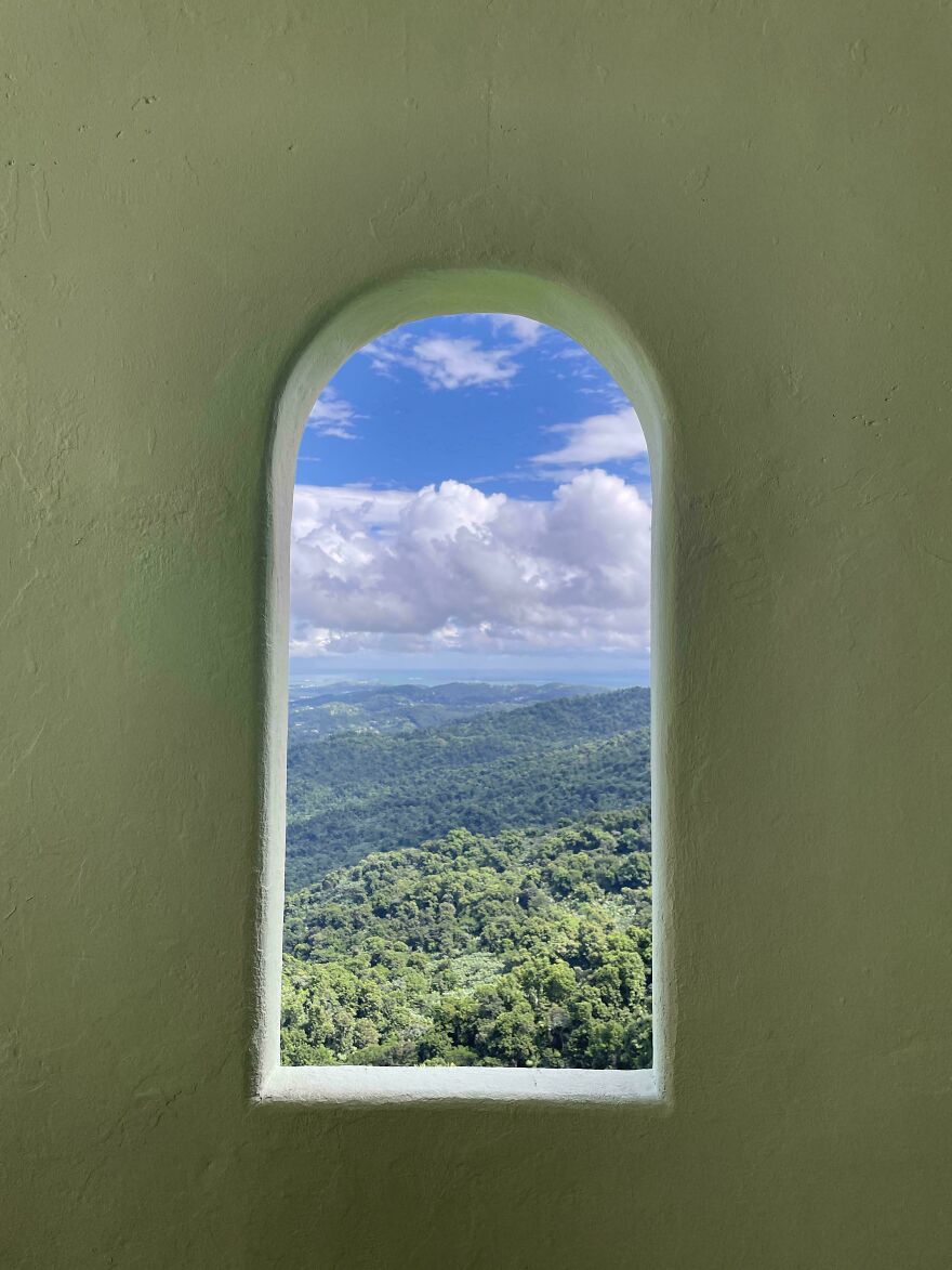 A picturesque landscape framed by an arched window, showcasing accidental art with lush greenery and a cloudy sky.