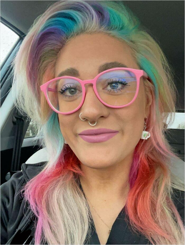 Person with vibrant, multicolored hair and pink glasses in a car, showcasing changing hair color.