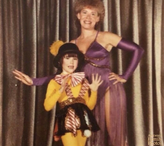 Awkward family photo with a child in a clown costume and woman in a purple dress, posing in front of a curtain.