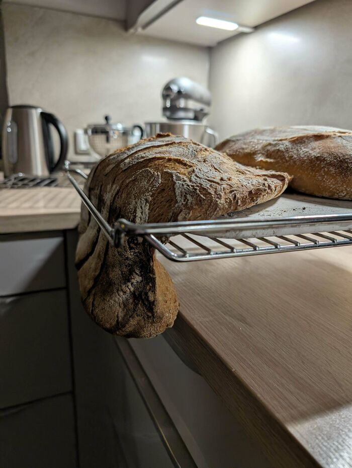 Bread loaf cooling on a rack with a unique expanding shape, showcasing creative baking skills.