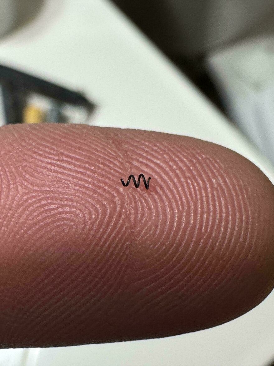 Tiny black squiggle on a fingertip resembling a sound wave.