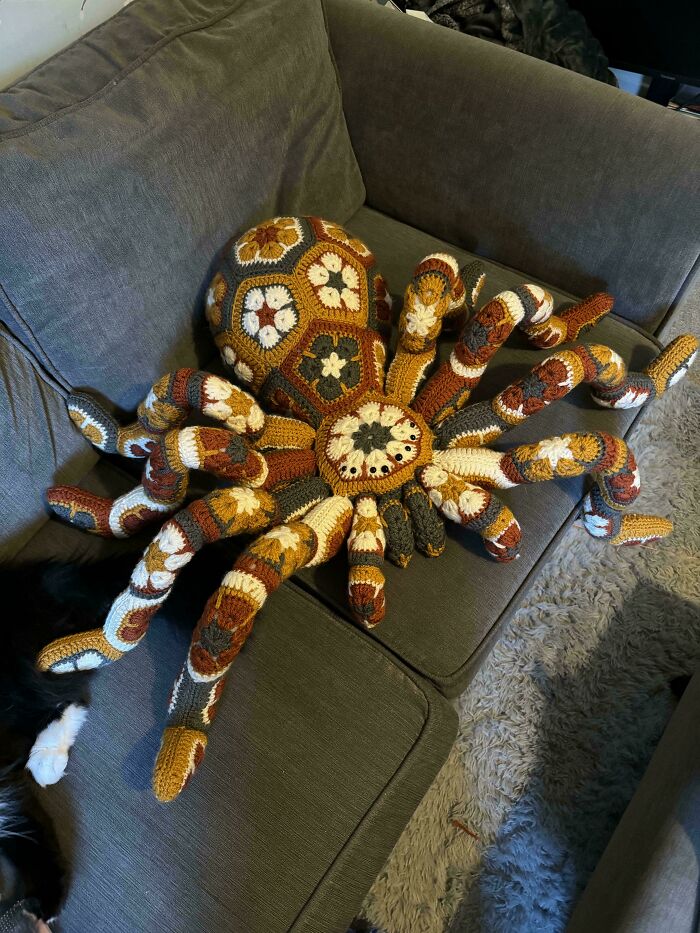 Crocheted octopus in warm colors on a gray sofa, showcasing incredible crochet craftsmanship.